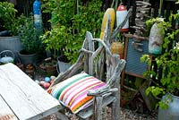 Chair made of drift wood - corner of cottage garden surrounded by vintage collection of galvanised planted containers and fishing floats against wooden fence  