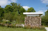 Modern shelter structure made using stone, wood and metal in wet grassland, damp area - Willow grove with Juncus effusesin in border