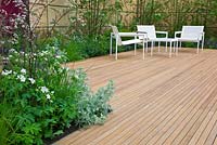 A wooden timber seating area in The Brewin Dolphin Garden at the RHS Chelsea Flower Show 2014. Planting includes: Artemisia absinthium 'Lambrook Silver', Anthriscus sylvestris 'Ravenswing', Geranium and Deschampsia cespitosa 'Pixie Fountain'.