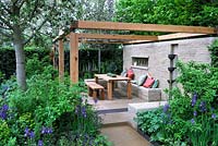 Outdoor seating and dining area with open pergola, wooden table and chairs with wall mounted water feature 
