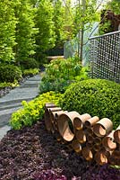 Honeycomb structure of cylindrical corten steel and path made from slates set on edge in The SeeAbility Garden. Planting includes: Geranium 'Black Beauty', Heuchera 'Obsidian', Sambucus nigra 'Black Lace', Buxus sempervirens and Euphorbia.
