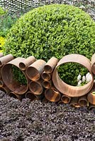 Honeycomb structure of cylindrical corten steel in The SeeAbility Garden. Planting includes: Buxus sempervirens