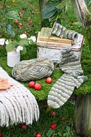 A rustic, moss covered bench with lunchbox, woollen throw, sock knitting, vase of snowberries and Observer books