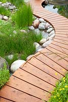 Trailfinders Australian Garden, Chelsea Flower Show 2013. Curving slatted timber path by swimming pond with Eleocharis acicularis and Eleocharis palustris