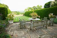Terrace framed with hydrangeas in pots, with lawn below edged by tall yew hedges, and meadow in the valley beyond. 