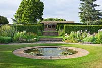 Circular pond in the lawn with view through hedges to the cotswold stone loggia