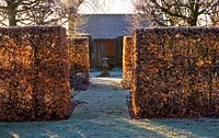 Winter garden in frost - view through beech hedging at dawn to sundial and summerhouse. Lawn with frost. Wollerton Old Hall, Shropshire