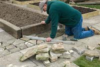 Man creating crazy paving to infill an area around raised beds