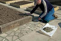Man creating crazy paving to infill an area around raised beds made with railway sleepers