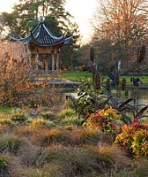Evening view across the lake to the Chinese pagoda with Hamamelis 'Aphrodite', Carex flagellifera and Carex ashimensis 'Evergold'