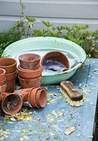 Brush, bowl of bubbly water and collection of dirty terracotta pots ready for cleaning