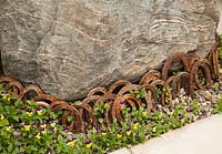 Large boulder with rusty horse shoes and planting of Viola 