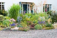 Hot colourful bed by gravel drive with Stipa gigantea, Eryngium, Dianthus, Iris, Brodiaea and Cistus 