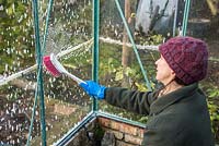Woman using soapy water and a brush to clean greenhouse windows