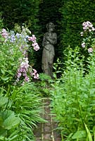 Stone statue of a girl, maiden in the niche of  a Taxus - yew hedge. Rosa 'Ballerina'  Suffolk by brick path. July