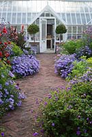 Central brick path in the walled garden is framed with asters, dahlias, euphorbia, Verbena bonariensis and leads to Alitex greenhouse door framed by standard clipped bay. 