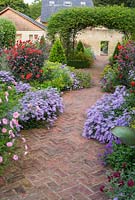 Central brick path in the walled garden is framed by asters, dahlias, euphorbia, Verbena bonariensis and clipped bay pyramids and runs underneath a central rose arch clothed with Rosa banksiae. 