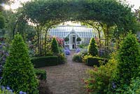 Central brick path in the walled garden passes beneath a central rose arch clothed with Rosa banksiae, and is edged with asters, dahlias, euphorbia and clipped bay pyramids as it leads toward the Alitex greenhouse. 