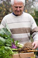 Man holding a crate of home grown vegetables. Carrots, leeks and kohl rabi.
