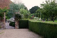 Formal country garden with clipped hedge, ornamental conifers, Malus, Eucalyptus and late summer planting with wooden bench