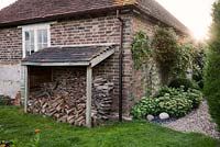 Logs and kindling stacked up in country garden with gravel path and Sedum
