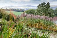 View across the Grasses Parterre. Corcosmia 'Lucifer' seedheads, Miscanthus sinensis  'Malepartus', Sorbus hupehensis - Veddw House Garden, Monmouthshire, Wales, UK. October. 
