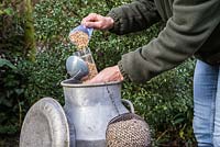 Refilling a clean birdfeeder with seed from a milk churn