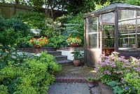 Garden view with Spirea 'Candlelight' Nasturtium 'Firebird' in terracotta pot, garden seat and hexagonal greenhouse