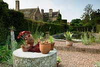 Swimming pool garden with mill stone table - containers with succulents  - houseleeks. Cothay Manor, Greenham, Somerset, England summer, late June garden 