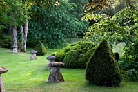 Stone ornaments in informal garden with green yew pyramid topiary - Cothay Manor, Greenham, Somerset, England summer late June garden 