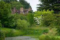 Cothay Manor, Greenham, Somerset. Lake with yellow flag iris and house in distance 

