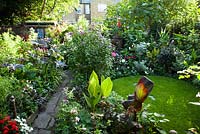 Wide view of late summer garden with lawn showing potting shed and Canna 'Striata' with other exotic border flowers 