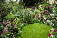 Wide view of late summer garden with lawn showing potting shed. Plants include Hibiscus, Ricinus, Petunia's Canna 'Striata', Canna 'Tropicanna' with other exotic border flowers
