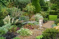 Formal garden in late summer with blue painted wrought iron bench, old sundial, gravel paths, roses, herbaceous perennials and view to lawns with box hedging and Yew topiary.