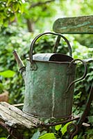 Rusty old watering can on old french chair, London, July