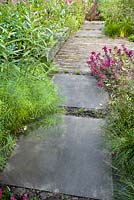 Pathway through borders in contemporary designed garden. Sporobolus heterolepis, Sedum Red Cauli, Amsonia hubrichtii. 