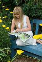 Woman relaxing on garden bench whilst reading magazine