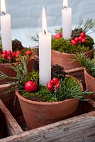 Candles in decorated terracotta pots with moss and berries in wooden trug.