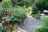 Spiral reflexology design made of pebbles, surrounded by summer borders. 