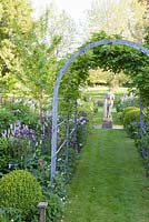 Decorative metal pergola and summer planting of Persicaria, Aquilegia, Sweet Rocket with stone statue beyond. The Old Rectory, Dorset