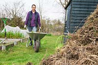 Woman pushing wheelbarrow of waste towards a compost heap