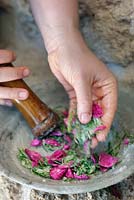 Using a pestle and mortar to create a spa treatment of rose petals, rosemary and salt 