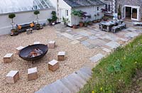 Patio with table and chairs and gravel seating area with large square wooden blocks for seats and fire cauldron