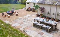 Patio with table and chairs and gravel seating area with large square wooden blocks for seats and fire cauldron
