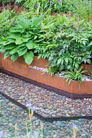 Pebble lined water feature with rusted metal border. Hosta hyacinthina. Garden: A Garden for First Touch at St George's. Designer: Patrick Collins. Sponsors: St George's Hospital Trust, Tendercare, Landscape Associates.