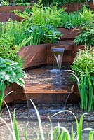 A Garden for First Touch at St Georges: Detail of stream contained by corton steel sides with hostas, ferns and iris - Sponsors: St Georges Hospital and Medical School, Tendercare, Landscape Associates 2014 RHS  Chelsea Flower Show garden awarded Silver Gilt medal