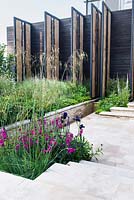 The Cloudy Bay Garden. View of stairs and tall oak wall which is creating a 'charred edge' of the garden amoung Iris 'Deep Black',Gladiolus italicus byzantinus and stipa gigantea.' Chelsea Flower Show 2014