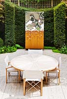 Table and chairs on terrace with sculpture and hedging 