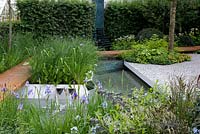RBS Waterscape Garden, RHS Chelsea Flower Show 2014, Gold Medal. Pool fed by spouts in raised sides. Plants include Iris sibirica 'Gerald Darby', Deschampsia cespitosa, Angelica atropurpurea
