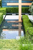 Detail of pool edged with clipped box with wooded wall in contrasting stains. The Extending Space. RHS Chelsea Flower Show 2014. Silver-Gilt medal. 